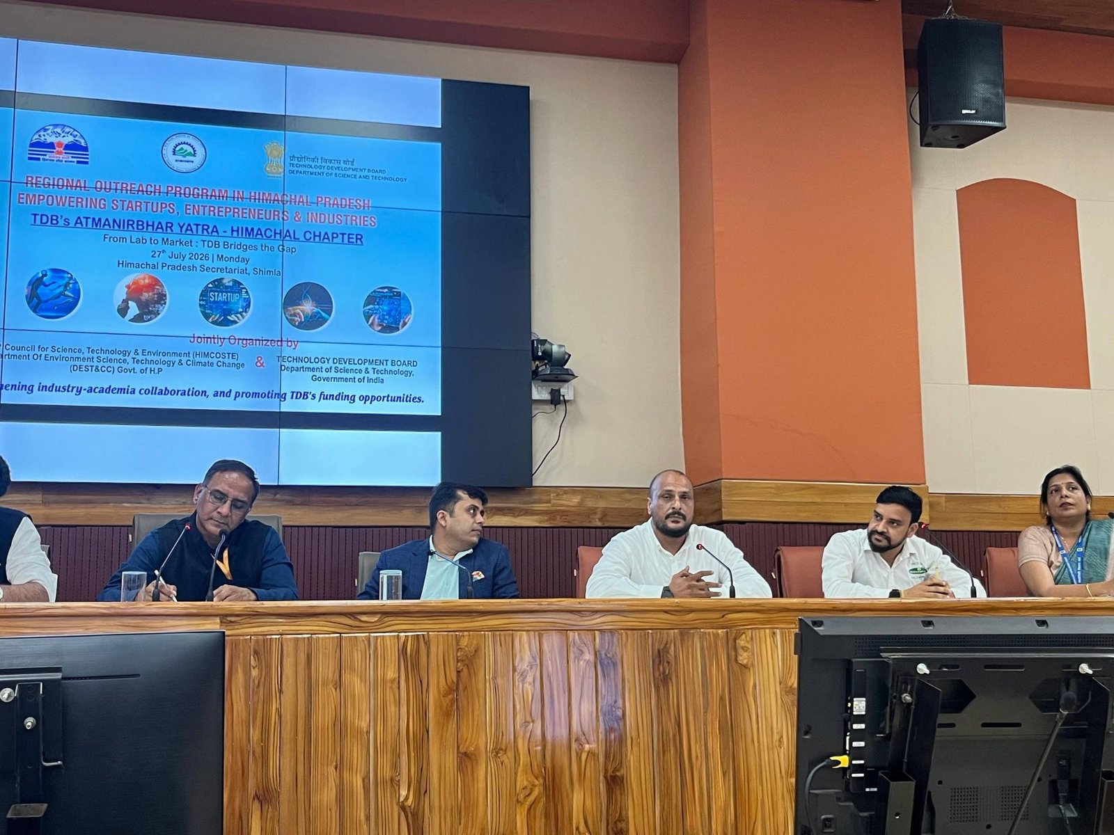 Chandan Vaidya of iIoTs speaking from a panel table at the Himachal Pradesh Secretariat in Shimla, with four other panellists seated alongside him. The screen behind shows the programme slide for TDB's Atmanirbhar Yatra, Himachal Chapter — a regional outreach programme for startups, entrepreneurs and industries, jointly organised by HIMCOSTE, the state Department of Environment Science, Technology and Climate Change, and the Technology Development Board of the Department of Science and Technology.